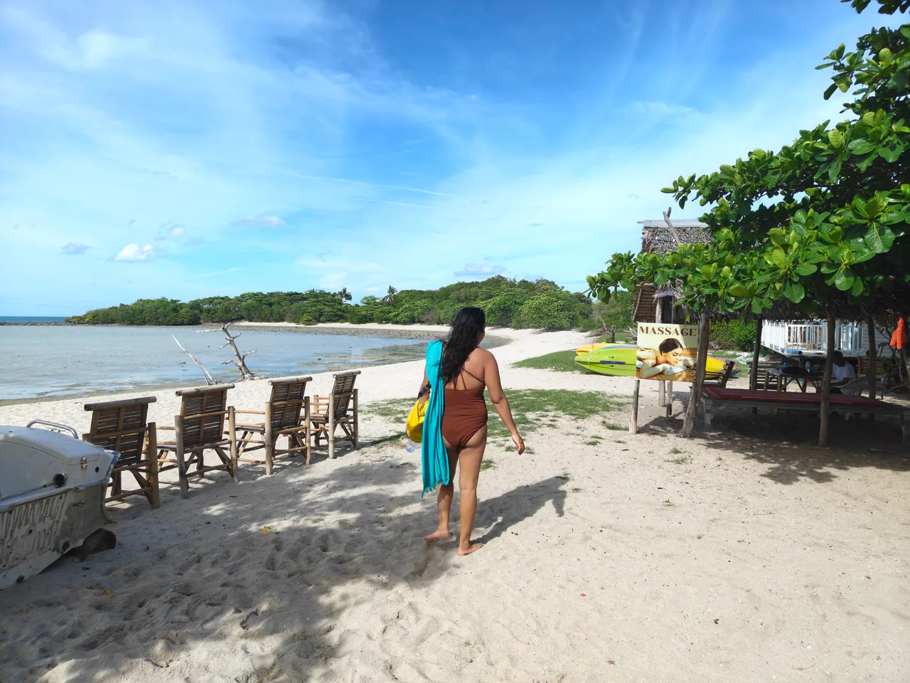 A visitor walking along the beach past seaside seating on Koh Madsum